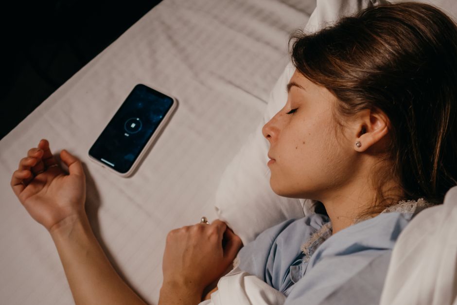 Les rêves lucides sont-ils scientifiquement prouvés? A woman sleeping peacefully in bed beside her smartphone, capturing a serene bedtime moment.