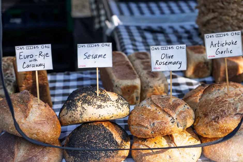 Assorted artisanal breads on display at a market stall, labeled with prices and ingredients.