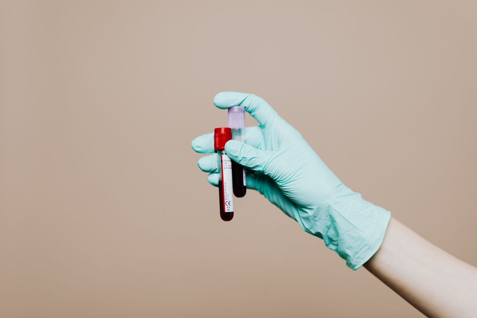 Le groupe sanguin influence-t-il vraiment la personnalité? Close-up of a gloved hand holding blood test tubes against neutral background.