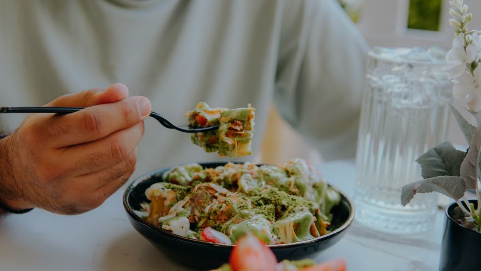 Manger tard le soir fait-il vraiment grossir? Close-up of a person eating creamy green sauce pasta at a table
