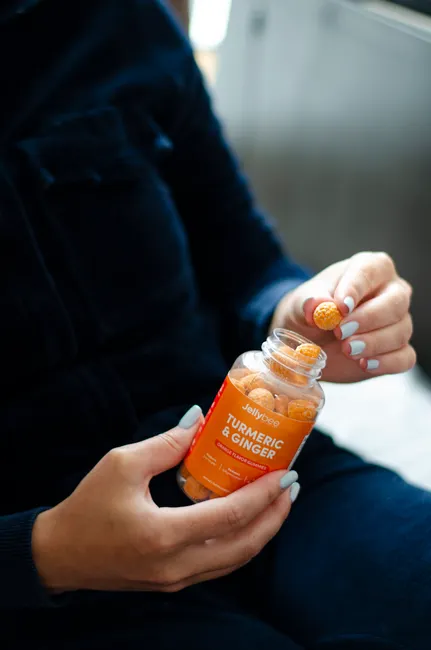 Close-up of a person holding turmeric and ginger gummies in a bottle with natural lighting.