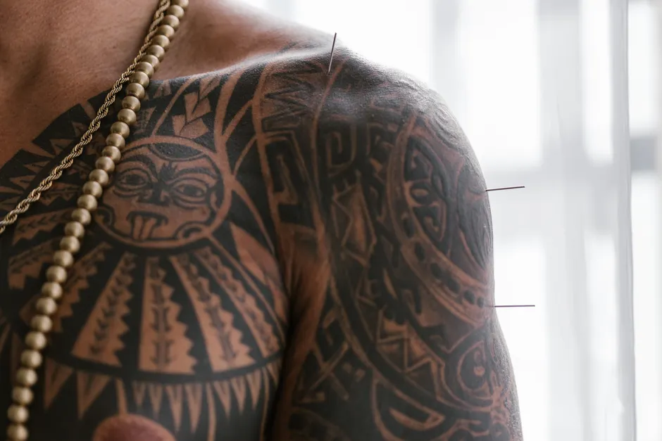 L’acupuncture soulage-t-elle vraiment la douleur? Close-up of a tattooed shoulder with acupuncture needles, showcasing alternative medicine practice.