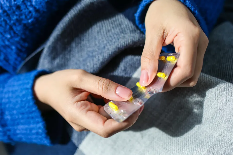Les antibiotiques guérissent-ils vraiment la grippe? Close-up of a woman's hands holding a blister pack with yellow pills, indoors.