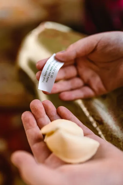 Close-up of hands holding a fortune cookie with a message, symbolizing tradition and luck.