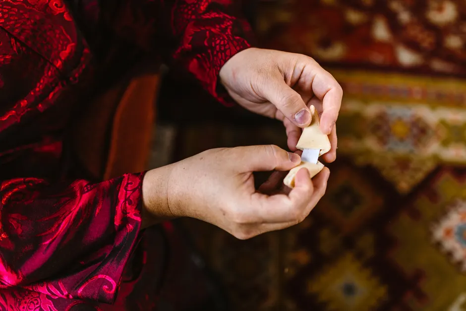 Close-up of hands opening a fortune cookie, dressed in ornate red fabric.