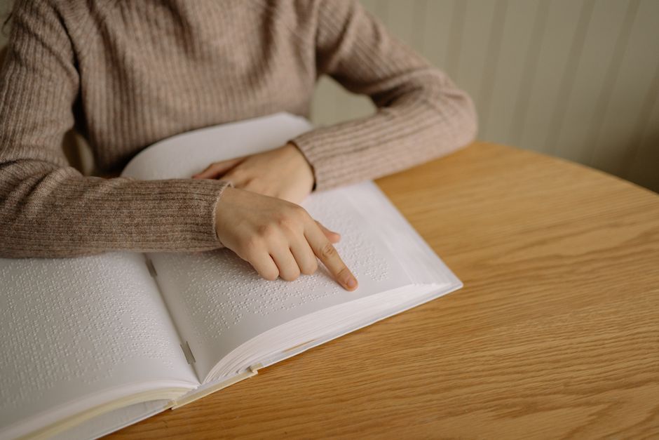 La dyslexie est-elle un handicap ou un don? Close-up view showing a hand reading Braille text, symbolizing accessibility and inclusion.