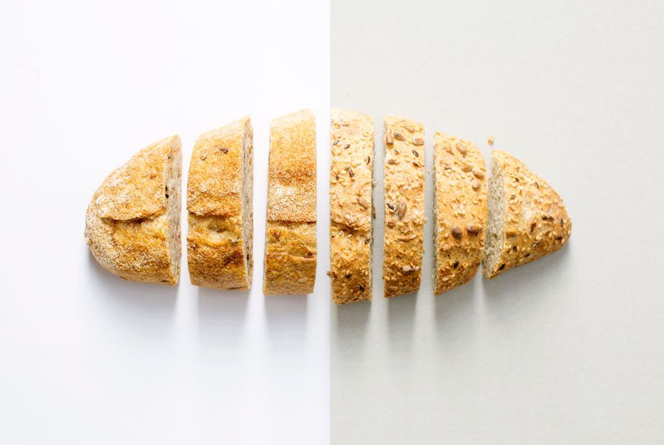 Le pain complet est-il vraiment toujours meilleur que le pain blanc? Freshly baked whole wheat bread sliced on a white background, showcasing its homemade texture.