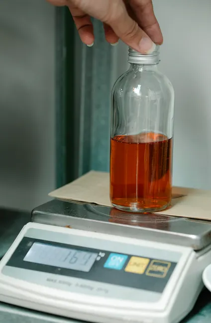 Glass bottle containing liquid being weighed on a digital scale in a laboratory setting.