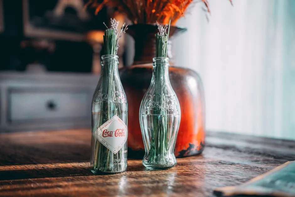 Coca-Cola contenait-il vraiment de la cocaïne? Le verdict selon l’époque Glass Coca Cola bottles used as vases in a rustic decor setting on a wooden table.