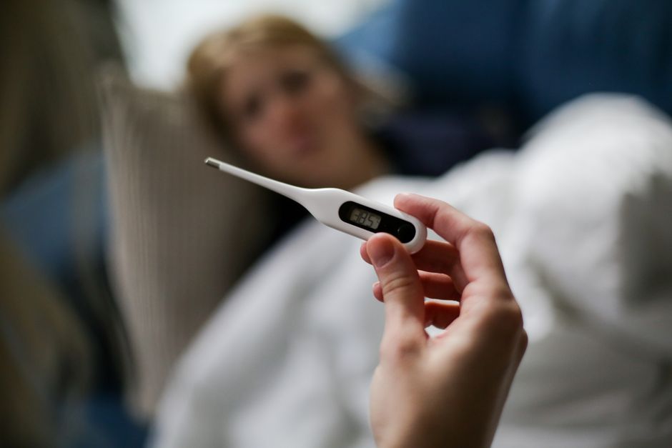 Peut-on vraiment attraper deux fois le même virus? Hand holding a digital thermometer with blurred background of a sick person.