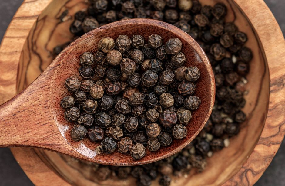 Le poivre noir a-t-il vraiment des propriétés médicinales? High-quality macro shot of black peppercorns in a wooden spoon on a bowl.