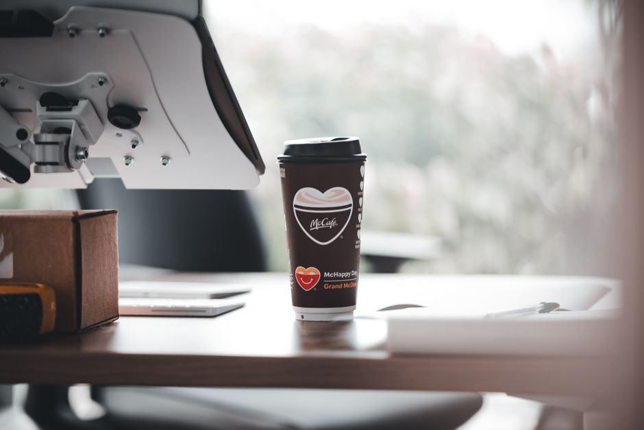 Le café empêche-t-il vraiment de grandir? McCafe branded coffee cup on a modern office desk, creating a relaxed work ambiance.