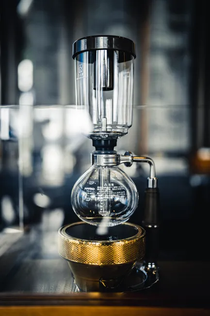 Modern syphon coffeemaker with glass brew chamber and bottom bowl placed on wooden counter in contemporary coffee shop on blurred background