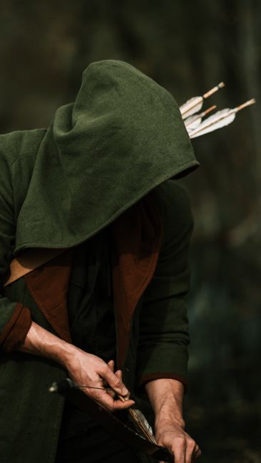 Mysterious archer in green hood draws an arrow, forest setting, medieval style.