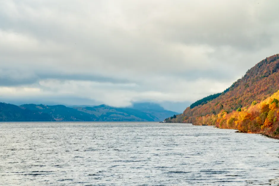 Scenic view of Loch Ness with autumn foliage and cloudy sky, perfectly capturing the essence of nature in fall.