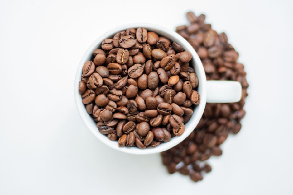 Le café torréfié contient-il vraiment du furane? Top view of a coffee cup brimming with roasted coffee beans on a white background.