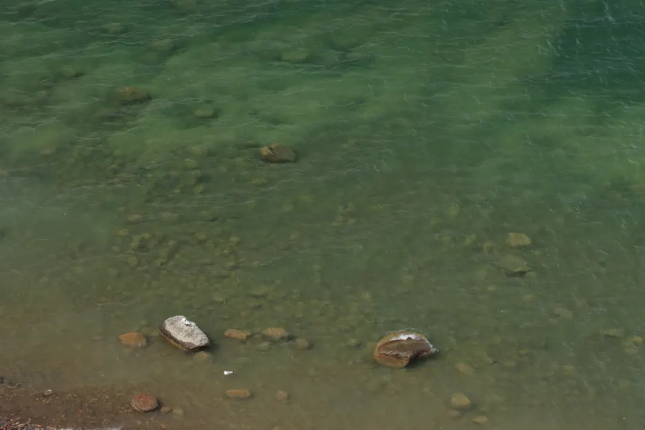 Tranquil beach scene with shallow green water revealing a rocky seabed.