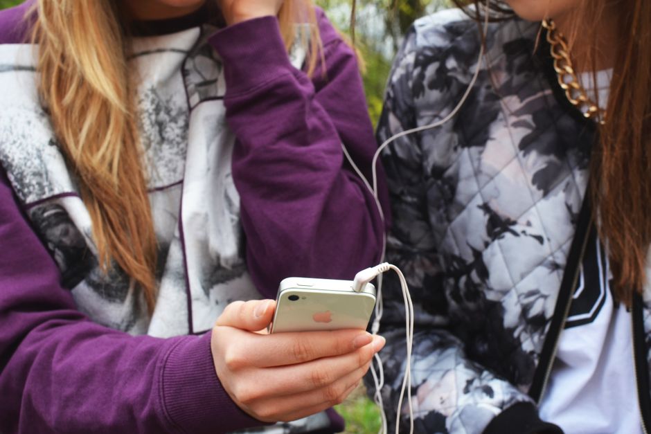 Two young women sharing music using a smartphone and earphones while enjoying time outdoors.
