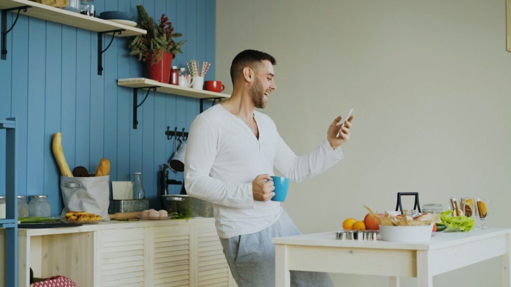 Retrouver son énergie : et si votre fatigue demandait autre chose qu’un stimulant ? Man dancing in kitchen holding coffee and phone
