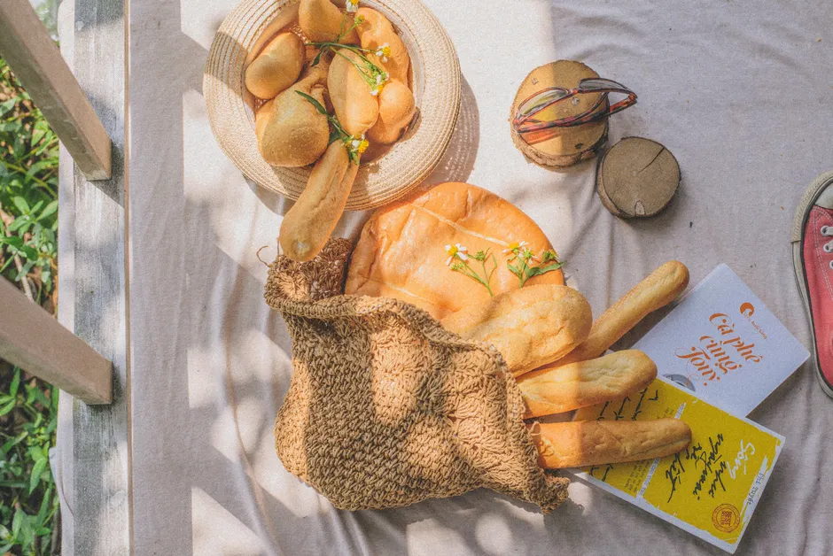 Marie-Antoinette a-t-elle vraiment dit « qu’ils mangent de la brioche »? A casual picnic setup with fresh bread and books in a sunlit garden setting.