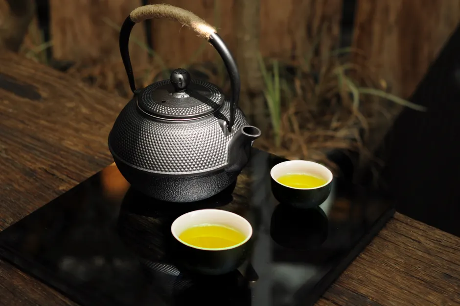 Le thé vert fait-il vraiment maigrir? A close-up view of a traditional black teapot with green tea cups on a rustic table, creating a serene scene.