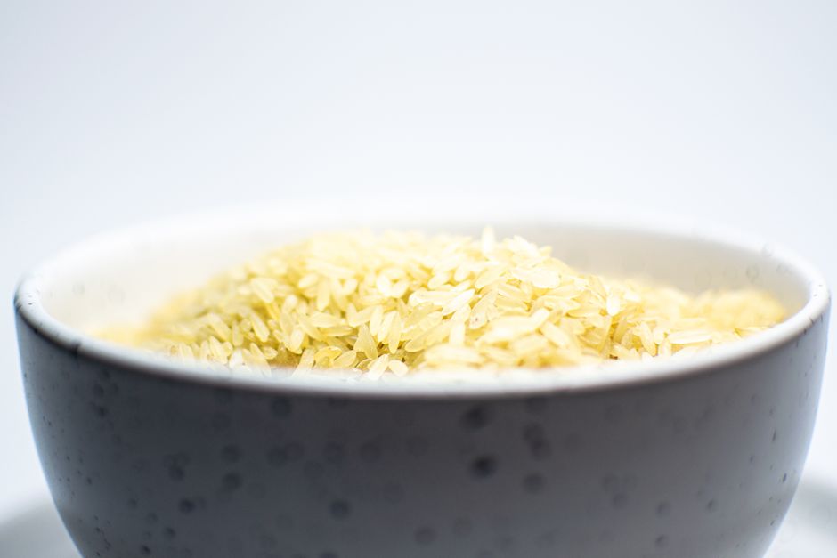 Réchauffer du riz est-il vraiment risqué? A close-up view of uncooked white rice in a speckled ceramic bowl on a light background.