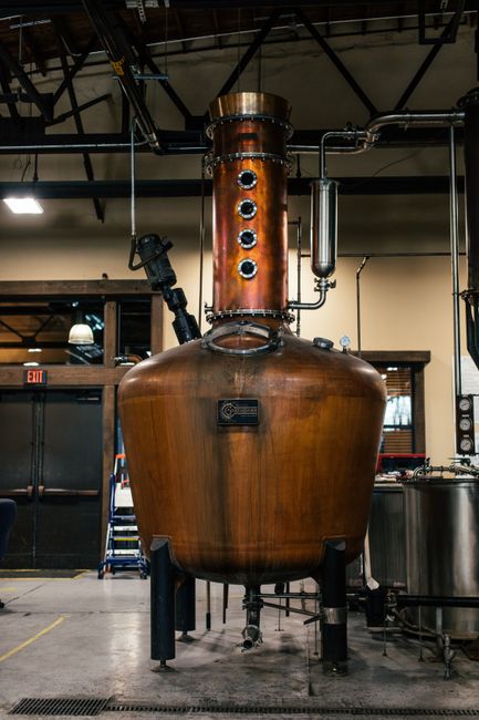 A copper distillation apparatus in an indoor industrial setting, showcasing brewery equipment.