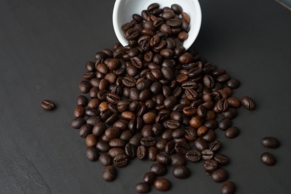 Le café torréfié contient-il vraiment du furane? A detailed close-up of roasted coffee beans spilling out of a white cup onto a dark surface.