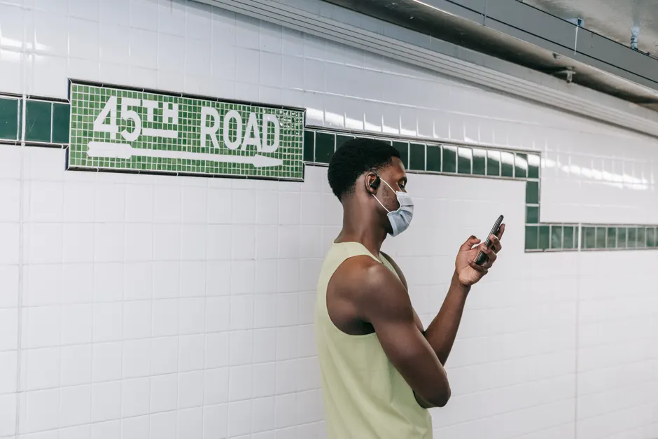 Les écouteurs peuvent-ils vraiment endommager l’audition? A man at 45th Road subway station uses his smartphone, wearing a protective mask.