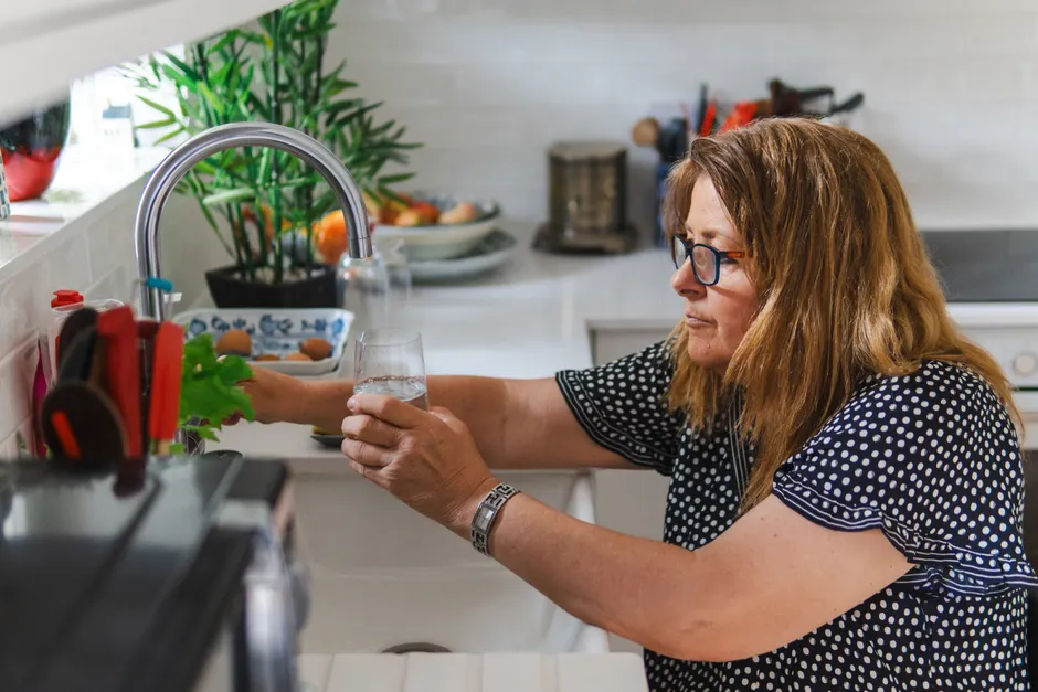 L’eau distillée est-elle dangereuse à boire? Le verdict des études A middle-aged woman filling a glass with water in a modern kitchen setting.