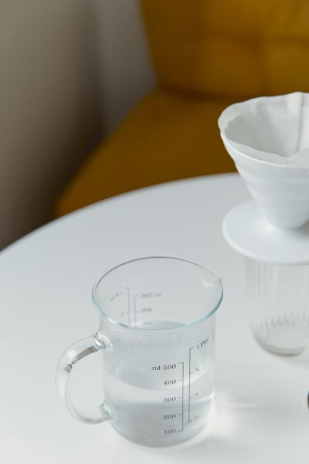 A minimalistic coffee preparation setup with a glass measuring cup and pour over filter on a white table.