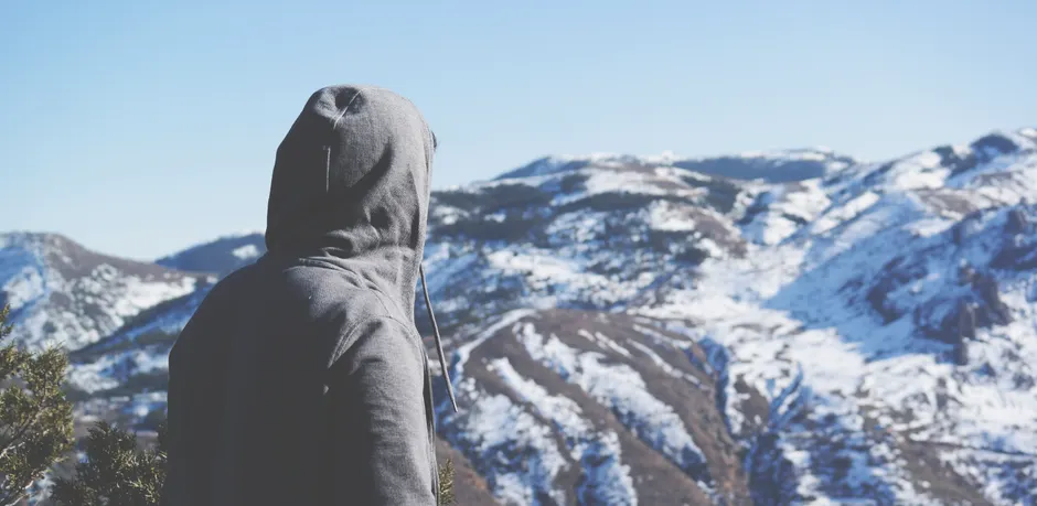 Peut-on attraper un rhume parce qu’on a froid? A person wearing a hoodie viewing a scenic and snowy mountainous landscape.