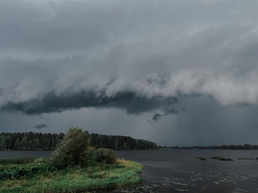 L’effet papillon peut-il vraiment provoquer une tempête? A powerful storm cloud formation looms over a tranquil lake and forest, capturing nature's dynamic beauty.