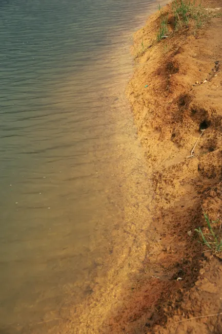 A tranquil aerial view of a sandy shoreline meeting serene waters under a clear sky.