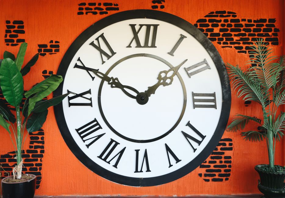 Manger tard le soir fait-il vraiment grossir? Le verdict des études A vintage-style wall clock with Roman numerals against a vibrant orange brick background.