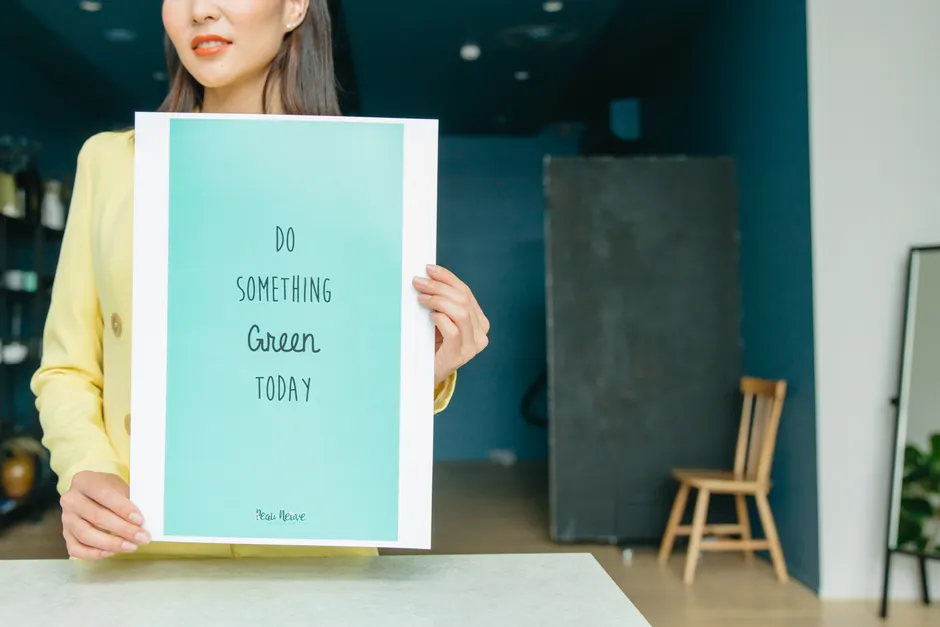 La pyramide alimentaire est-elle encore considérée comme valide? A woman holding a motivational green poster that says 'Do Something Green Today' indoors.