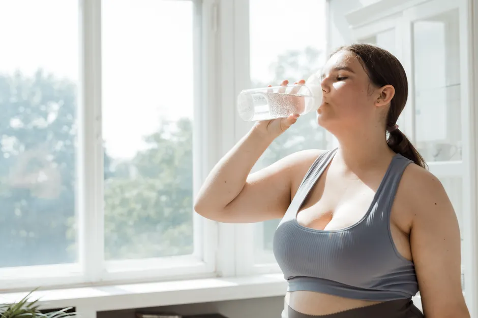 Active woman in sportswear drinks water indoors. Healthy lifestyle and hydration.