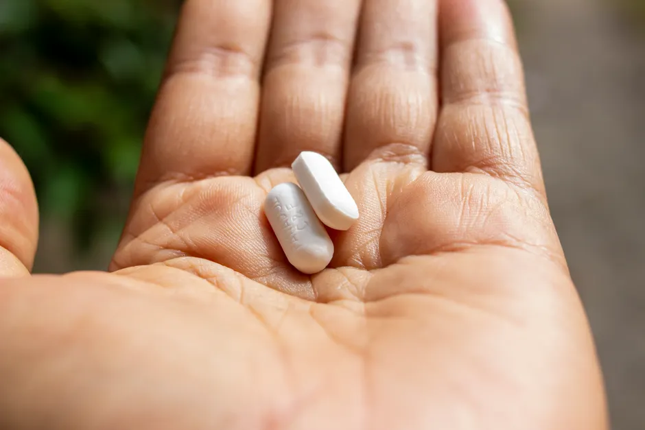 Les probiotiques améliorent-ils vraiment la santé intestinale? An intimate close-up of two pills held in a person's open palm against a blurred outdoor background.