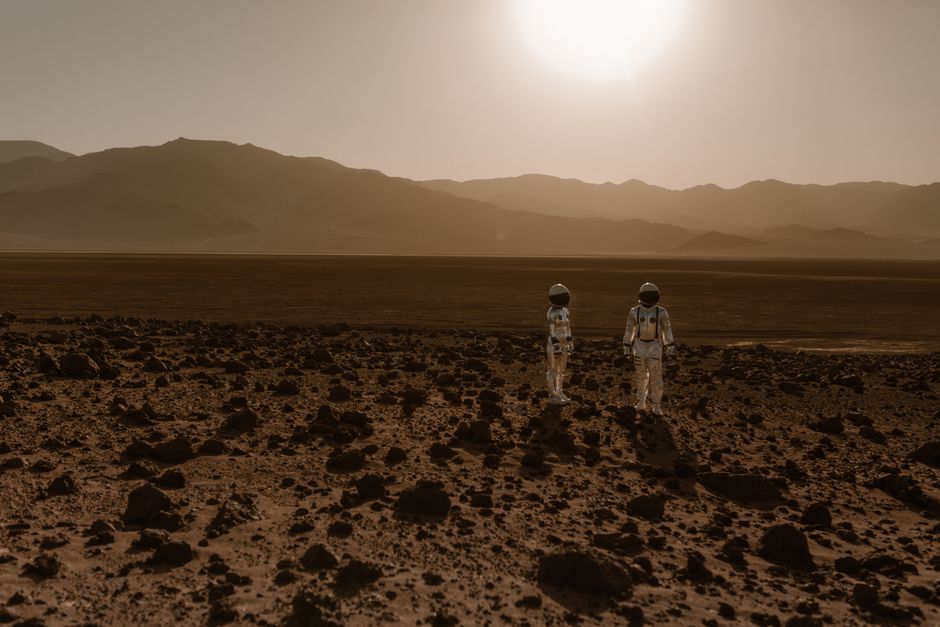 Mars a-t-elle vraiment abrité la vie? Astronauts in space suits explore a rocky, desert-like terrain resembling Mars at sunset.