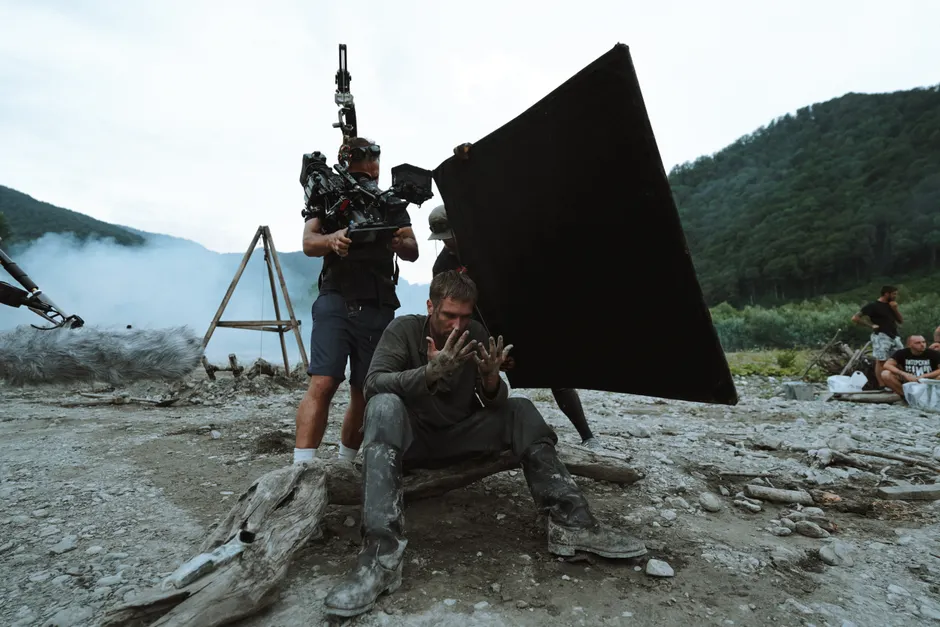 Behind-the-scenes view of film production with actors and crew on location outdoors.