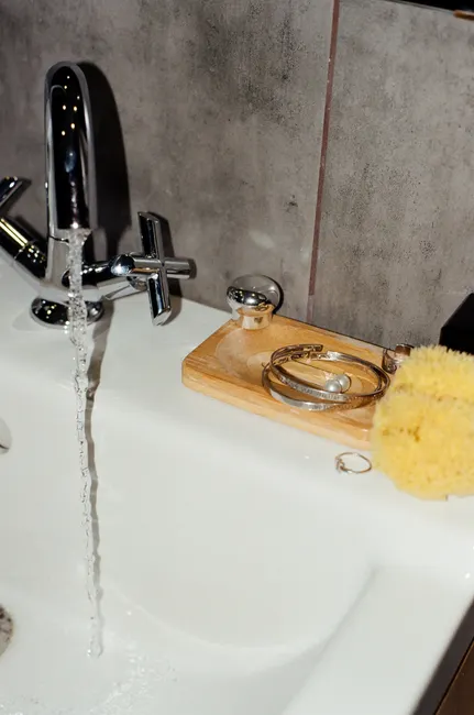 Close-up of a bathroom sink with running water, jewelry, and a sponge, highlighting luxury and style.