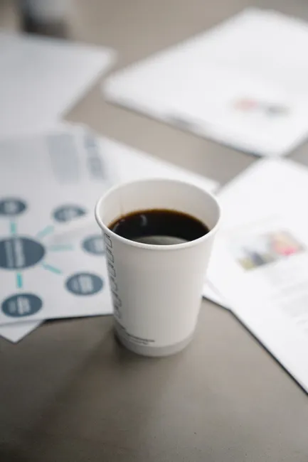Close-up of a disposable coffee cup on a desk surrounded by documents and charts.