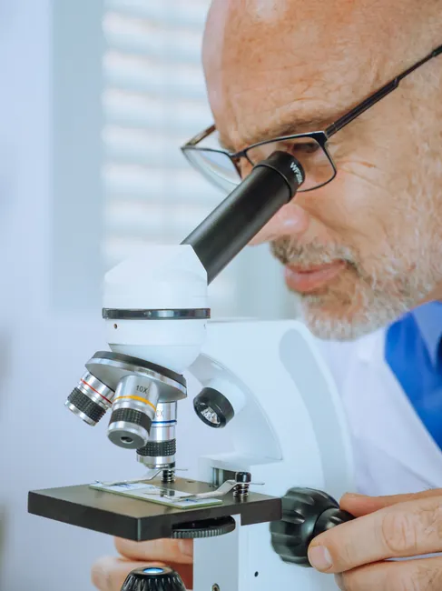 Close-up of a scientist analyzing a microscope slide in a laboratory.
