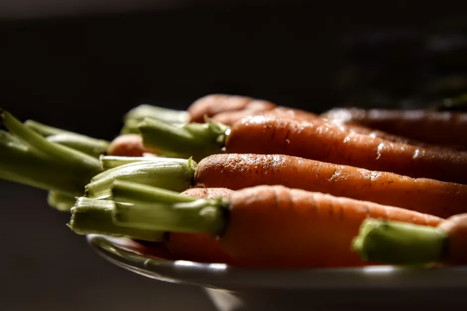 Les carottes améliorent-elles vraiment la vision nocturne? Close-up of fresh organic carrots with green tops in dramatic lighting, highlighting texture.