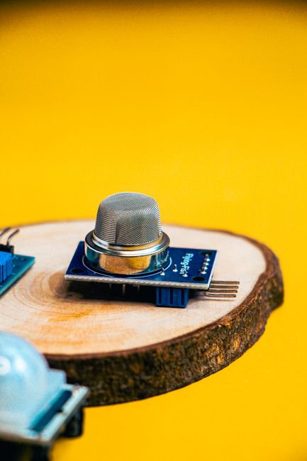 High-quality image of an electronic sensor placed on a round wooden base, contrasting with a vibrant yellow background.