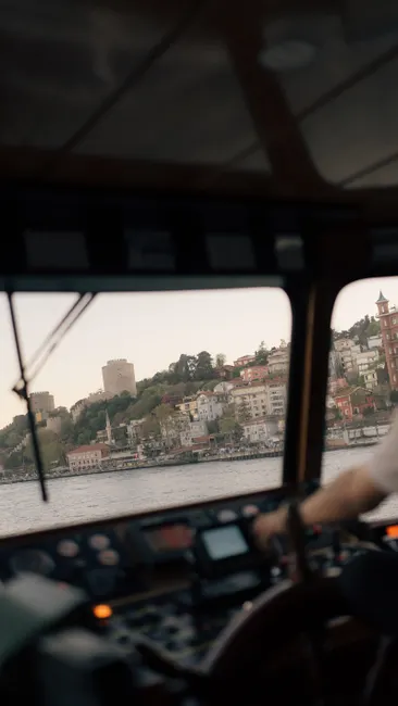 Interior of a boat cockpit with a view of a coastal town, showcasing navigation and sailing elements.