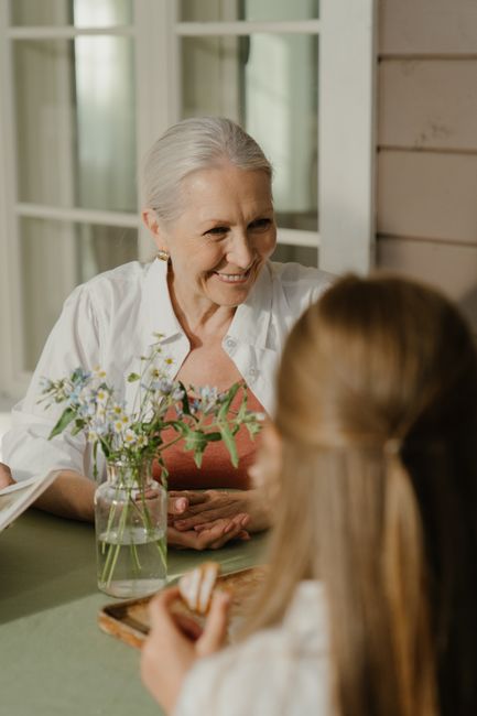 Senior woman with gray hair smiling and sitting indoors at a table with family.