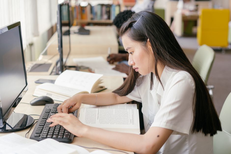 Teenager studying in a modern library with books and computer equipment.