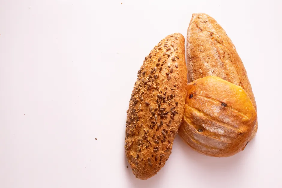 Le pain complet est-il vraiment toujours meilleur que le pain blanc? Top view of three freshly baked artisan bread loaves with seeds and crusty surfaces.