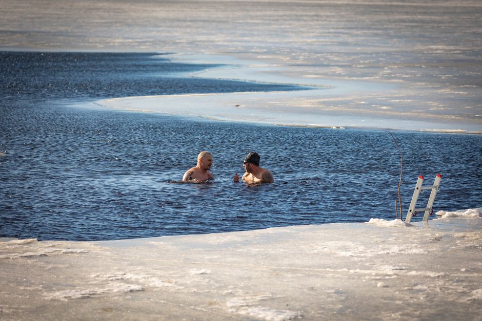 Les bains froids renforcent-ils vraiment l’immunité? Two men brave the cold for a swim in a partially frozen lake during winter.